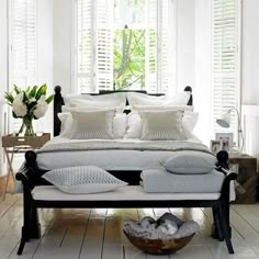 a bed with white sheets and pillows in a bedroom next to a basket full of flowers