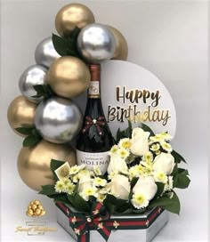 a bottle of champagne and flowers in a gift box with balloons on the wall behind it