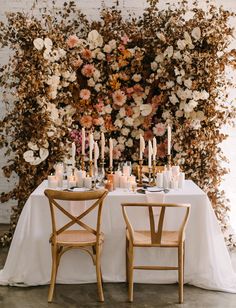 the table is set with candles and flowers on it, along with two chairs that are facing each other