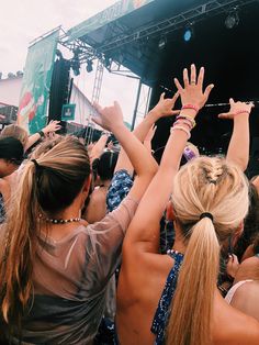 two women reaching their hands up in the air at an outdoor music festival or concert