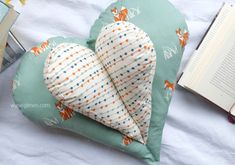 a heart shaped pillow sitting on top of a bed next to a book and cup