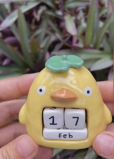 a yellow clock with a green face is held in someone's hand next to a plant