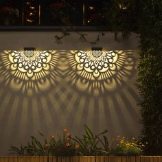 shadows cast on the side of a building with plants and flowers in front of it