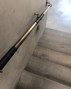 a black and silver pipe on the side of a wall next to some stairs with wooden handrails