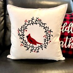 a pillow with a cardinal on it sitting next to a black leather chair and red plaid pillows