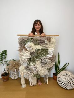 a woman holding up a large piece of art made out of paper and yarns