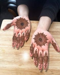 two hands with henna designs on them sitting on a wooden table next to each other