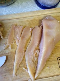 three pieces of chicken sitting on top of a wooden cutting board