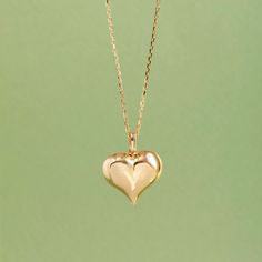 a small gold heart pendant on a chain with a light green backgroung