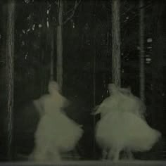 two women in white dresses are walking through the woods