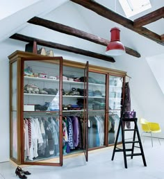 an open closet with clothes hanging on the wall and two stools in front of it