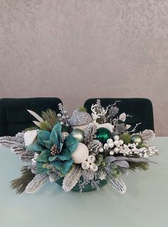 a green vase filled with silver and white flowers on top of a table next to a black chair