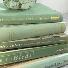 three books stacked on top of each other next to a glass vase with flowers in it