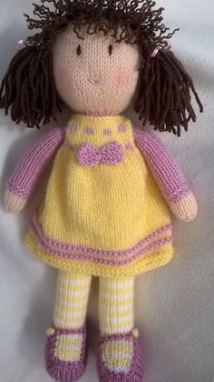 a knitted doll with brown hair wearing a yellow dress and pink shoes on a white background