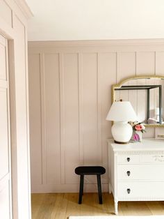 a white dresser sitting next to a mirror on top of a wooden floor in a room