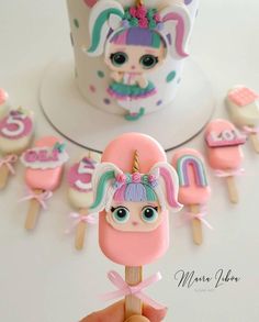 a hand is holding a popsicle with an image of a unicorn on it and other decorations in the background