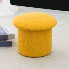 a yellow ottoman sitting on top of a bed next to a stack of books and magazines