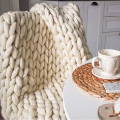 a knitted blanket sitting on top of a table next to a cup and saucer