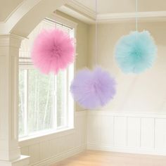 three fluffy pink and blue pom - poms hanging from the ceiling in an empty room