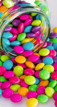 a jar filled with colorful candy beans on top of a white table next to a pile of other candies