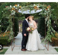 a bride and groom are kissing under an arch decorated with greenery at their wedding