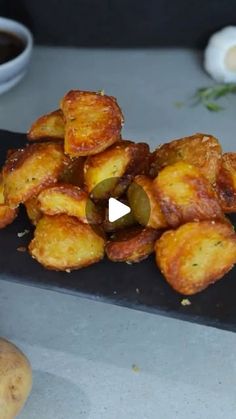 some fried food on a black plate next to dipping sauce and two small white bowls