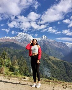 a woman standing on top of a mountain next to a lush green forest covered hillside