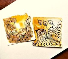 two square coasters with designs on them sitting on top of a wooden table next to each other