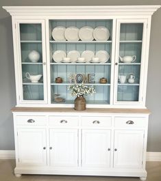 a white china cabinet with glass doors and plates on top