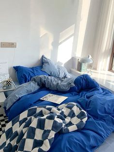 an unmade bed with blue comforter and checkered blanket on it in a white room