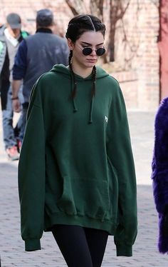 a woman in a green hoodie and black leggings walking down the street