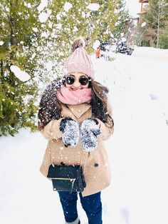 a woman standing in the snow with her hands on her chest and mittens up