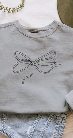 a t - shirt with a bow on it sitting next to denim shorts and a necklace