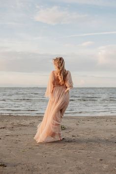 a woman standing on top of a sandy beach next to the ocean wearing a long dress