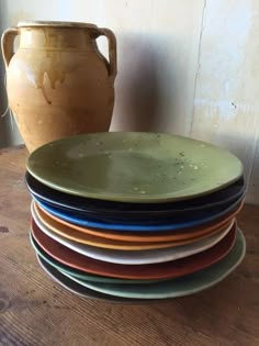 a stack of plates sitting on top of a wooden table next to a brown vase