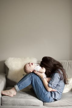 a woman sitting on top of a white couch holding a baby next to her face