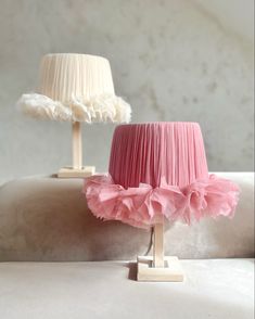 a pink lamp shade sitting on top of a wooden stand next to a white lamp