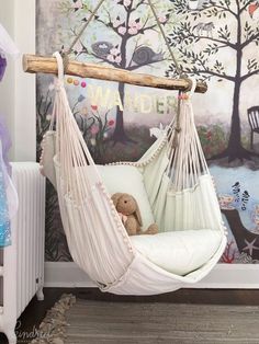 a white hammock chair with a teddy bear in it next to a wall mural