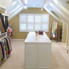 an attic bedroom with closets and clothes on hangers in front of the window