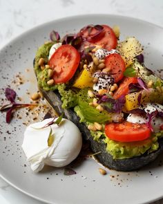 a white plate topped with an avocado and tomato sandwich