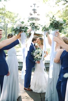 a bride and groom kiss as their bridal party takes place in front of them