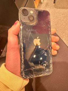 a person holding up an iphone with a cracked glass case on it's back