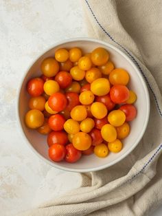 a white bowl filled with lots of orange and yellow tomatoes on top of a table