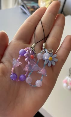 a hand holding three small necklaces with flowers on them and beads hanging from the ends