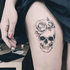 a woman's thigh with a skull and roses tattoo on it