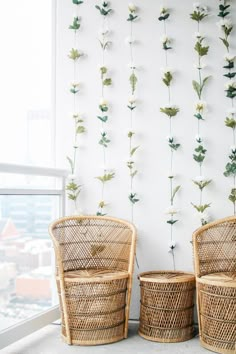 two wicker chairs sitting next to each other in front of a wall with plants on it