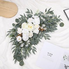 a bouquet of white flowers and greenery sits on a bed next to an open book