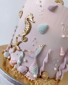 a pink and gold cake decorated with seahorses, seashells and pearls