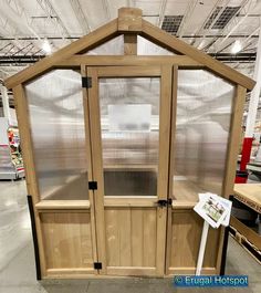 a large wooden greenhouse with glass doors in a warehouse or shop area, for sale