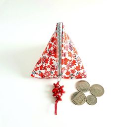 a small red and white flowered purse next to some coins on a white surface